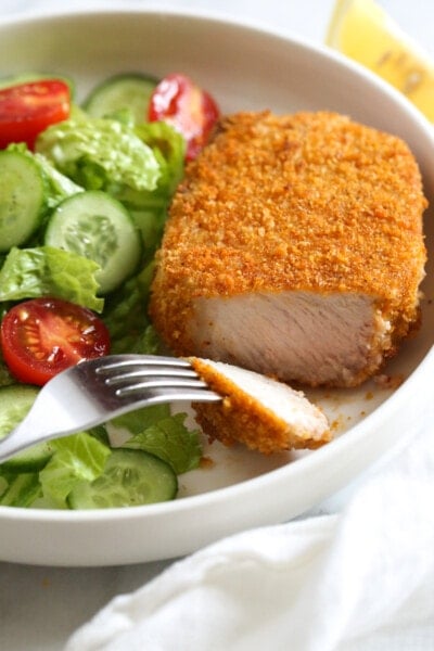 Breaded air fryer pork chops with lettuce, tomatoes, cucumbers, and a fork